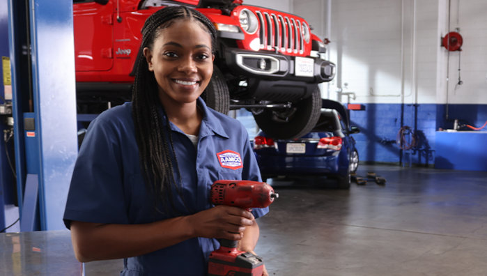 AAMCO Mechanic holding electric drill saw in front of lifting red Jeep car for fleet services